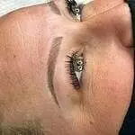 Christine Reynolds, a tattoo artist, is tattooing a woman's eyebrows.