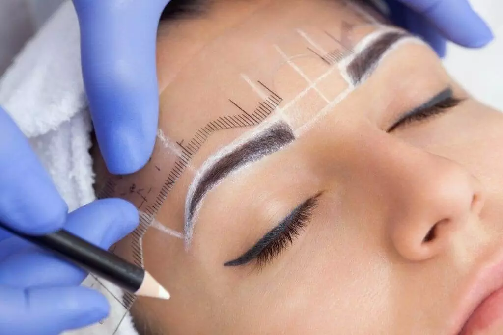 A woman getting her eyebrows microbladed at a beauty salon.