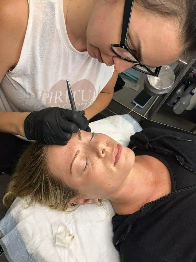 A woman receiving microblading for her eyebrows in a salon.