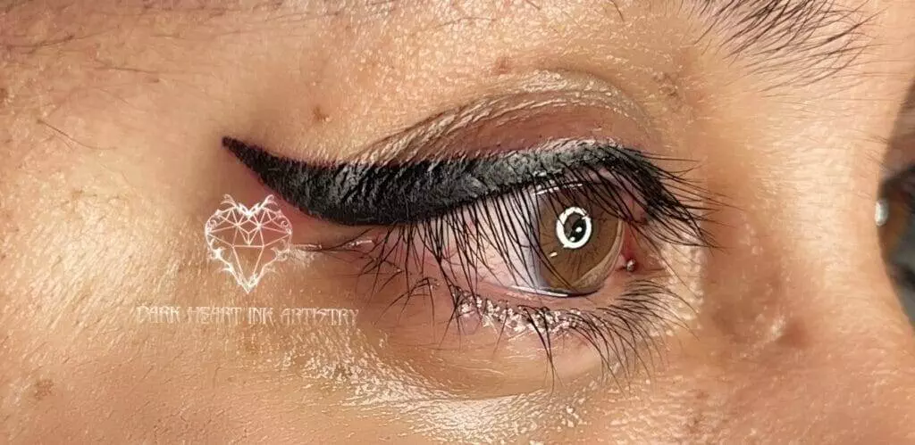 A close up of a woman's eye with black eyeliner enhanced by cosmetic tattooing.