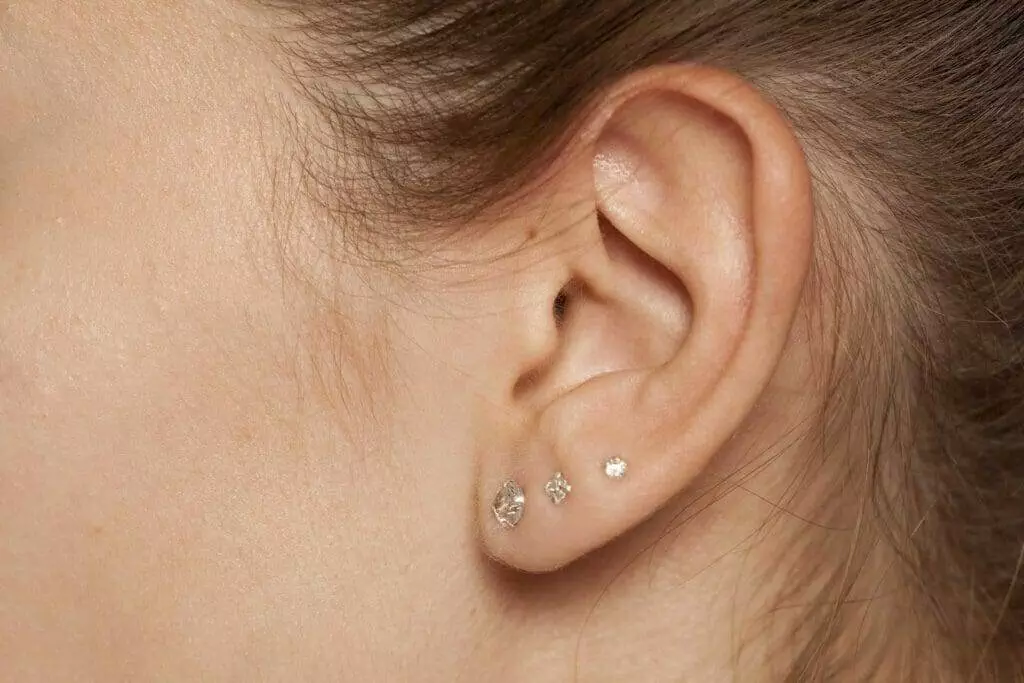 A woman's ear adorned with diamond piercings.