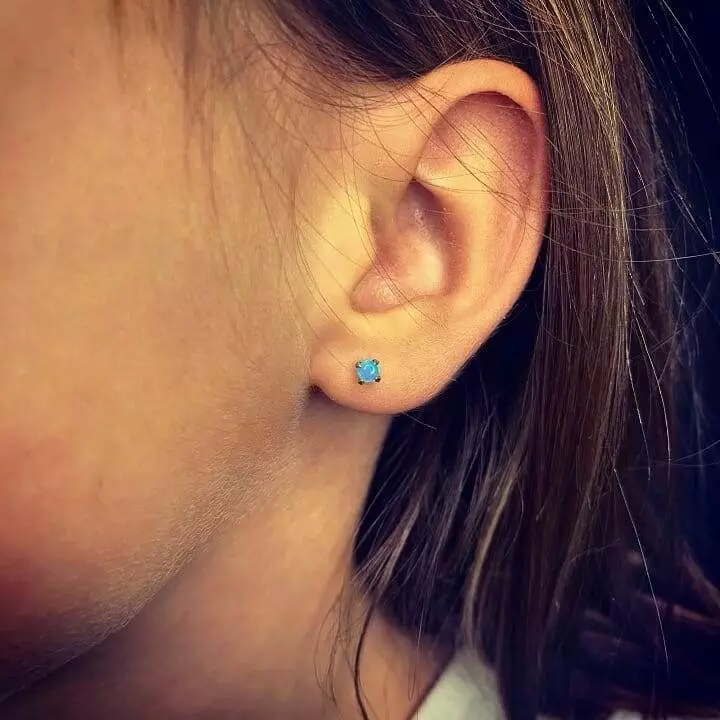 A girl's ear with a blue stud earring.