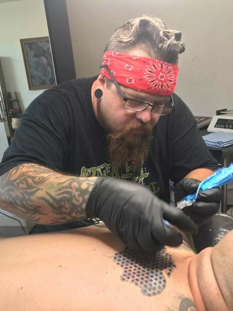 A man with a beard getting a tattoo on his FAQ.